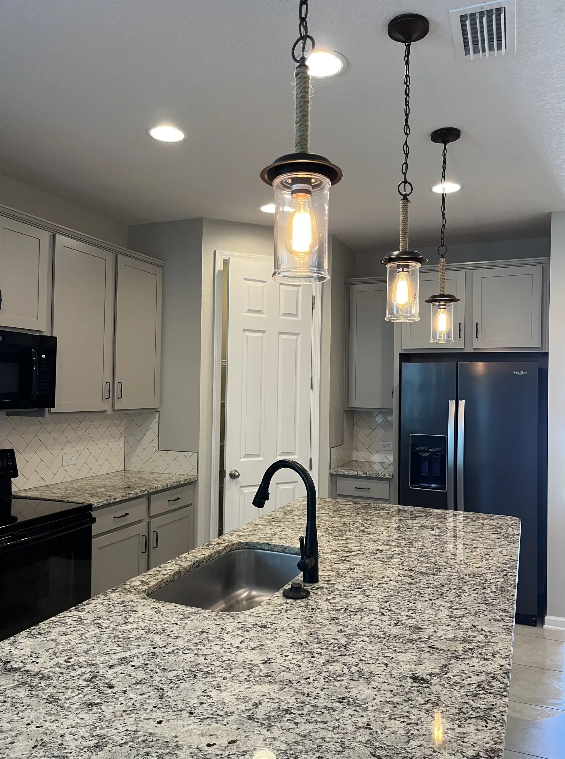 Spotless modern kitchen with granite countertops, clean sink, and hanging lights