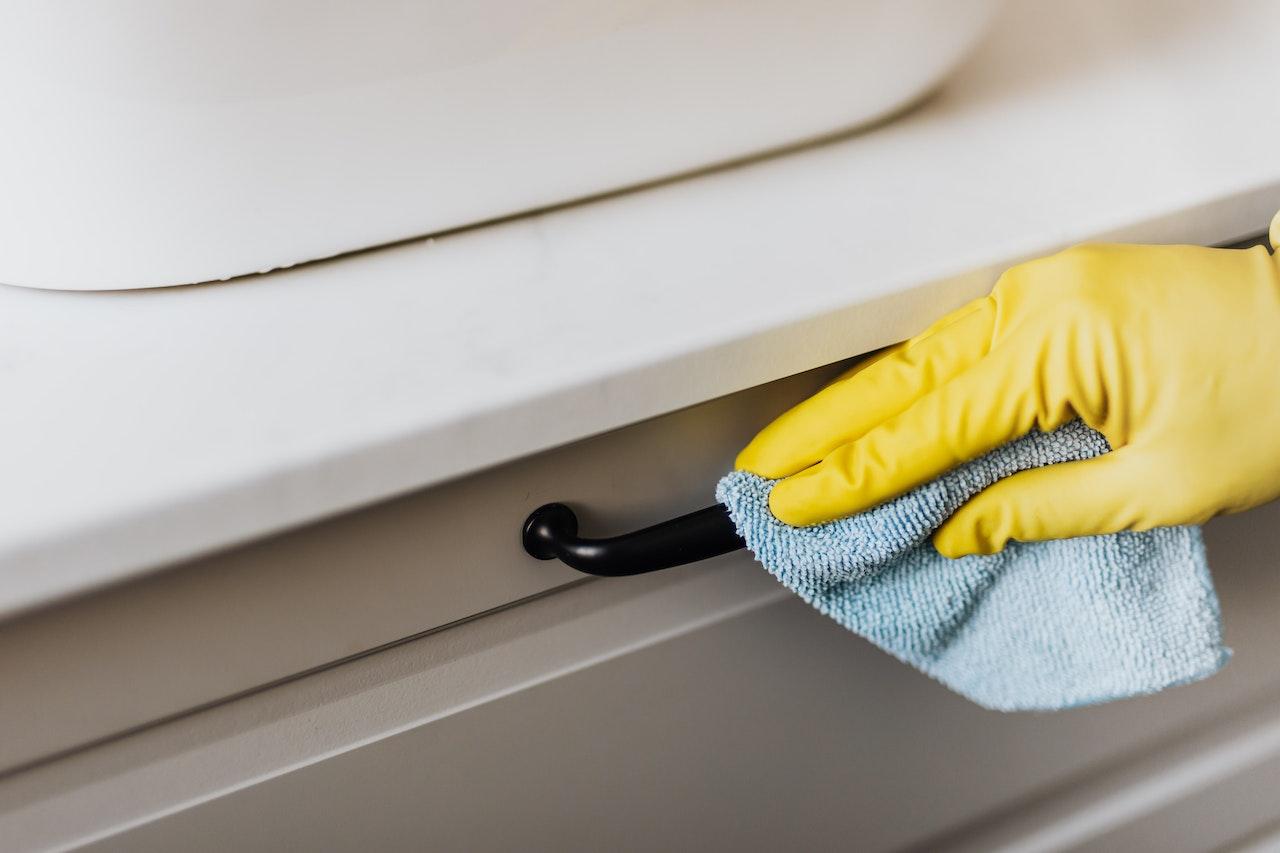 Person wearing yellow gloves wiping a cabinet handle with a blue microfiber cloth