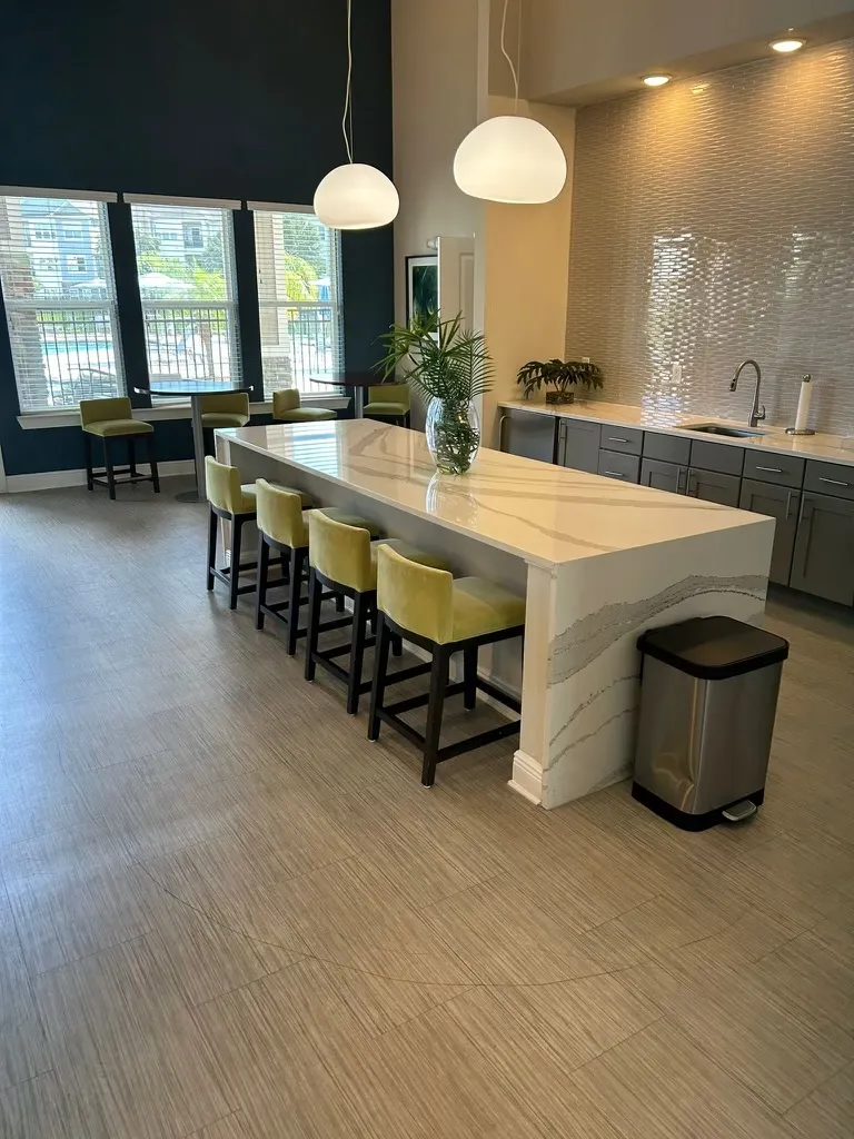 Clean kitchen and seating area with bar stools and a modern countertop in an apartment complex clubhouse