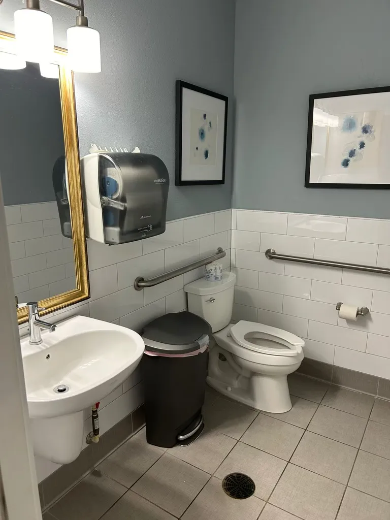 Clean and accessible restroom with modern fixtures, including a sink, toilet, and handrails in an apartment complex clubhouse