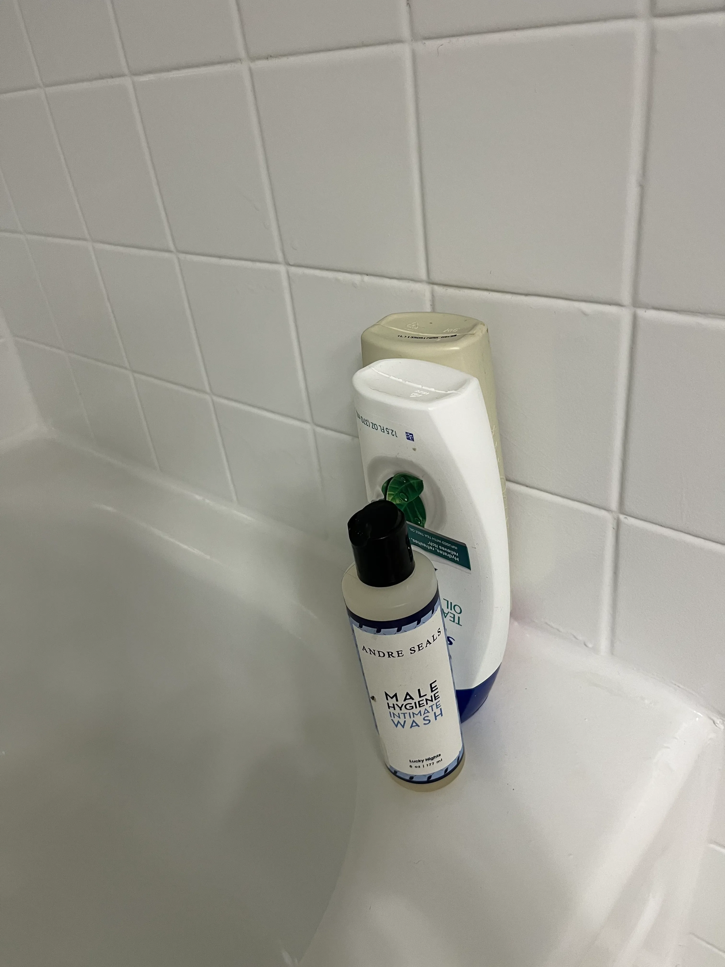 Two shampoo and hygiene bottles in a clean white-tiled shower corner in a residential bathroom